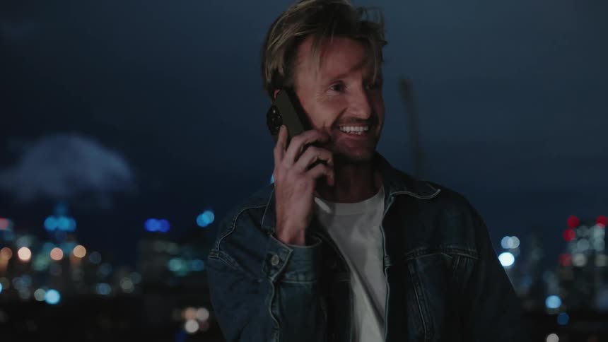 A man talking on his cell phone laughing and smiling with a city skyline in the background