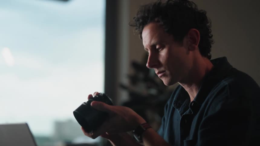 A man is sitting at his desk and evaluating a camera lens