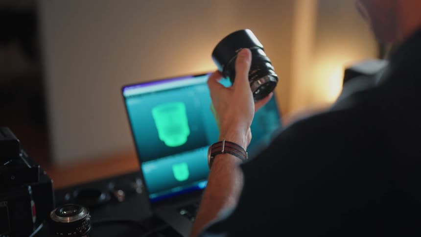 Man sitting at desk in front of laptop and dslr camera examining camera lens