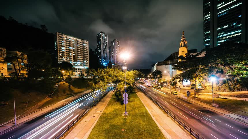 Traffic moves in and out of the busy city as lights in tall buildings turn on and off and clouds move across the night sky