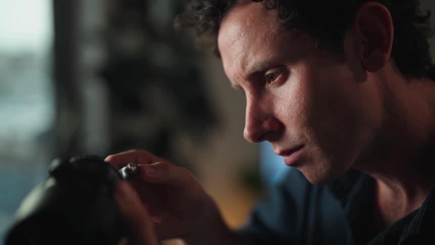 Man sitting at a desk holding a dslr camera lens and adjusting with a tool