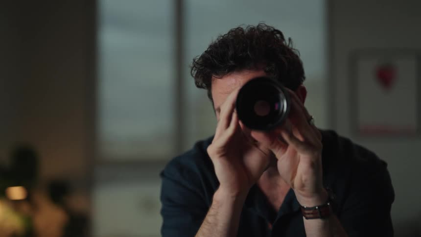 A man is sitting in his room and looking through a lens
