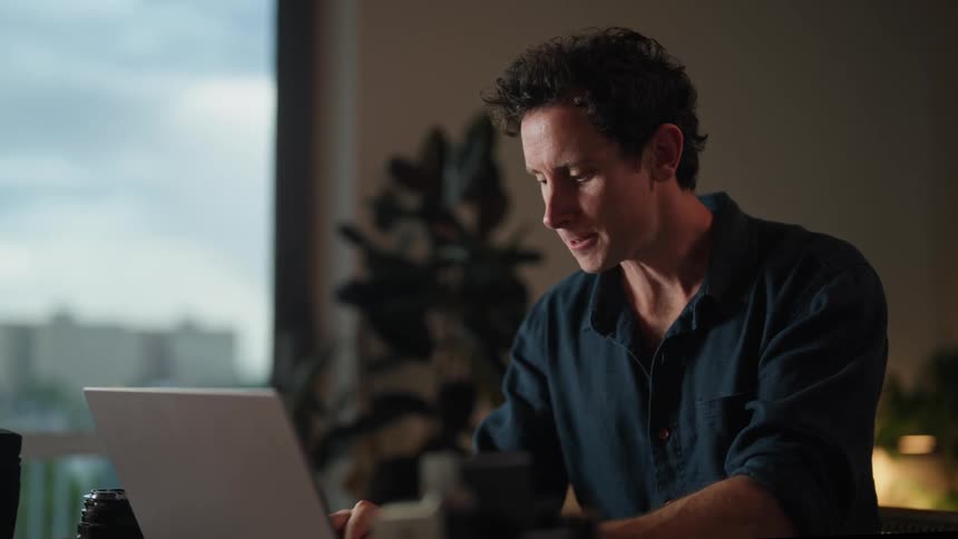 A man is typing on his laptop and drinking coffee