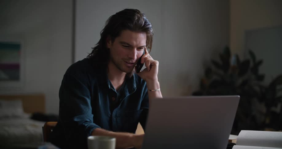 A man talks on the phone while working on his laptop