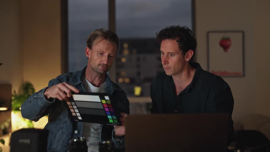 Two men looking over a print and talking while looking at a laptop