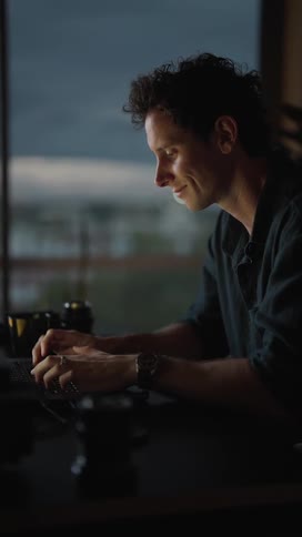 A man sitting typing on a laptop keyboard slightly smiling