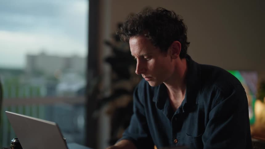 A man is sitting at his desk and typing on a laptop