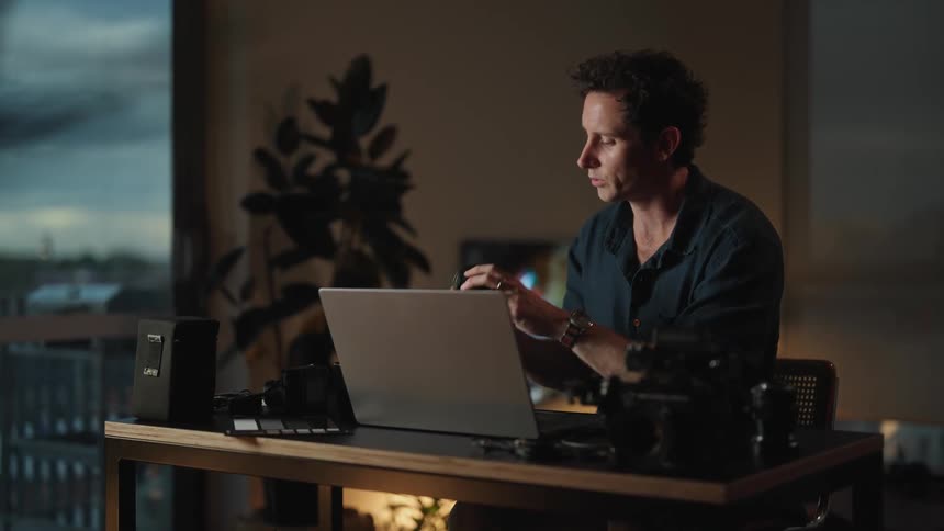 Man sitting at desk having zoom meeting and handling camera lens and camera equipment