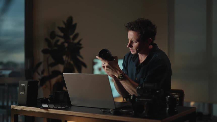 A man is showing a camera lens to someone on his laptop