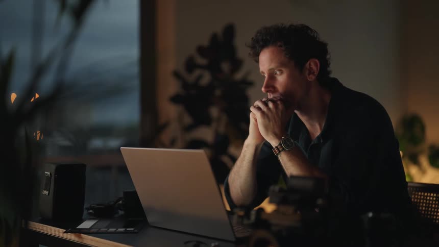 A man is drinking coffee and staring at his laptop