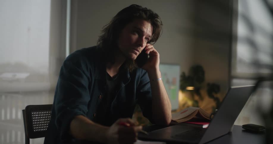 A man is sitting at a desk and talking on a phone
