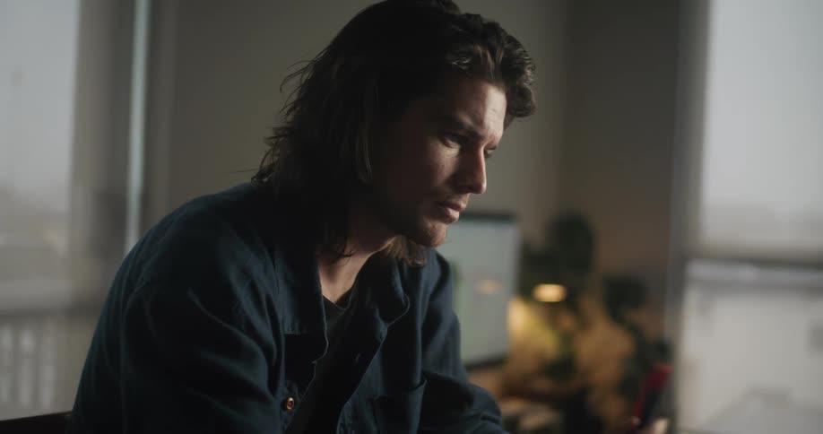 A man sitting at his desk typing on a laptop and looking contemplatively