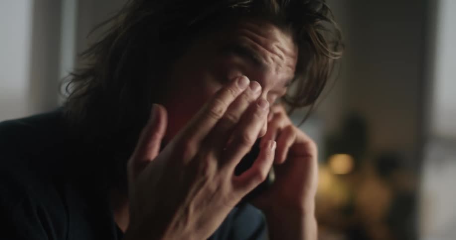 A close up of a mans face while he talks on the phone and rubs his eyes with his hand
