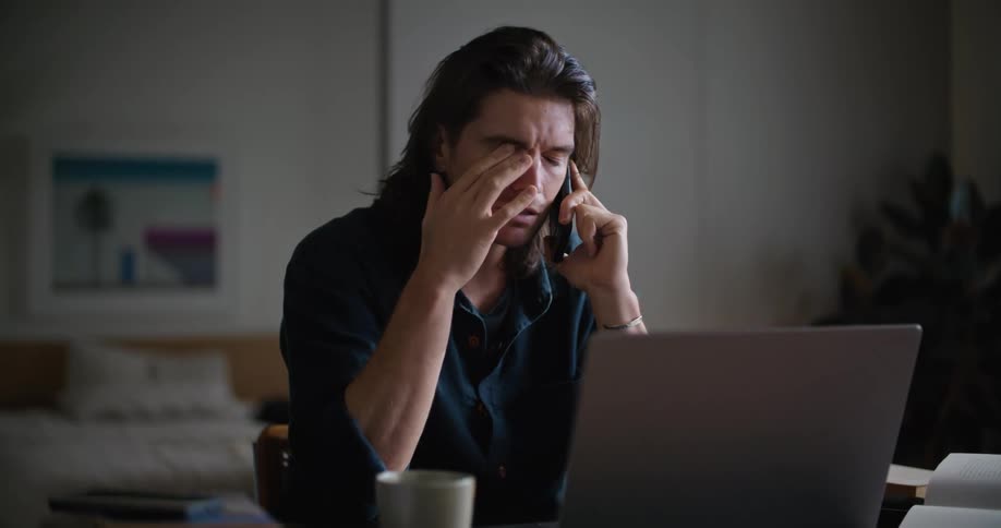 A man is talking on the phone at his laptop