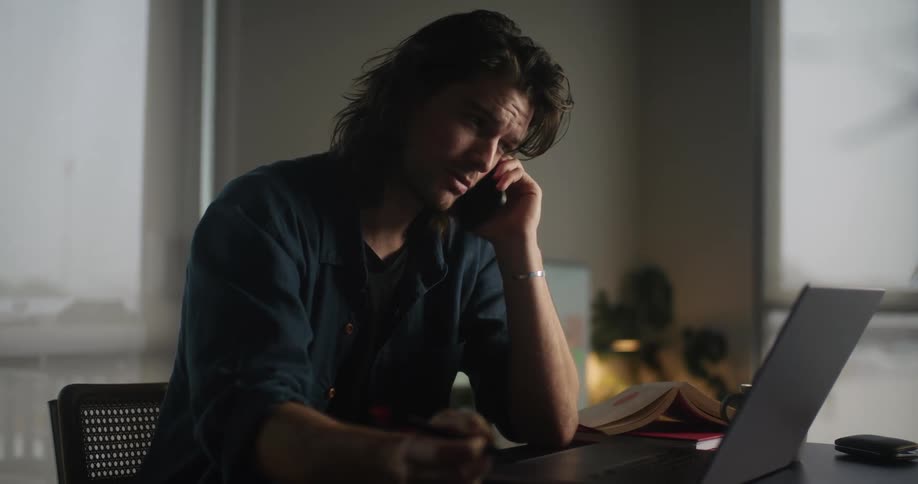 A man is talking on the phone and working on his laptop