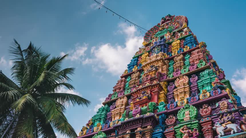 Pyramid covered in vivid multicolored carvings towers over palm tree