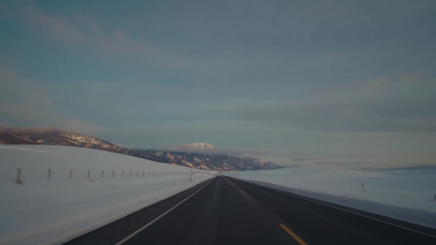 Traveling on a rural highway with snow on the roadside and mountains in the distance