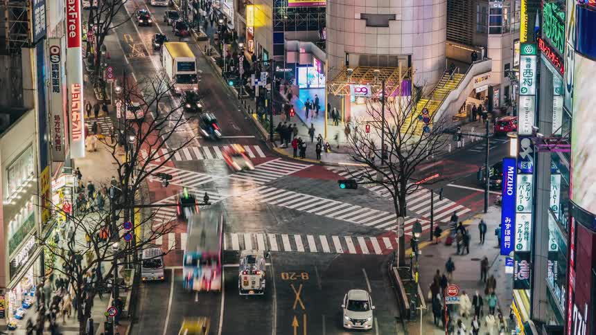 Pedestrians and traffic cross busy intersection in city near leafless trees