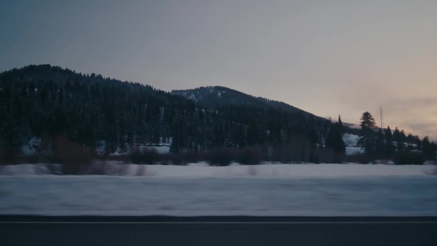 Traveling on a rural highway with snow on the roadside with forested mountains in the distance
