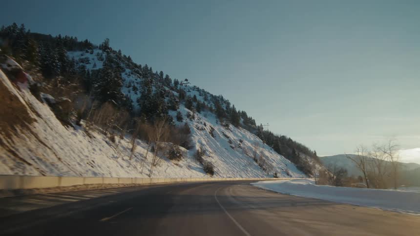Traveling on a curving mountain road with the sun shining low in the sky and snow on the slope