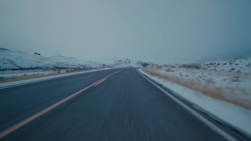 The camera moves forward along a two lane road that passes through an open landscape