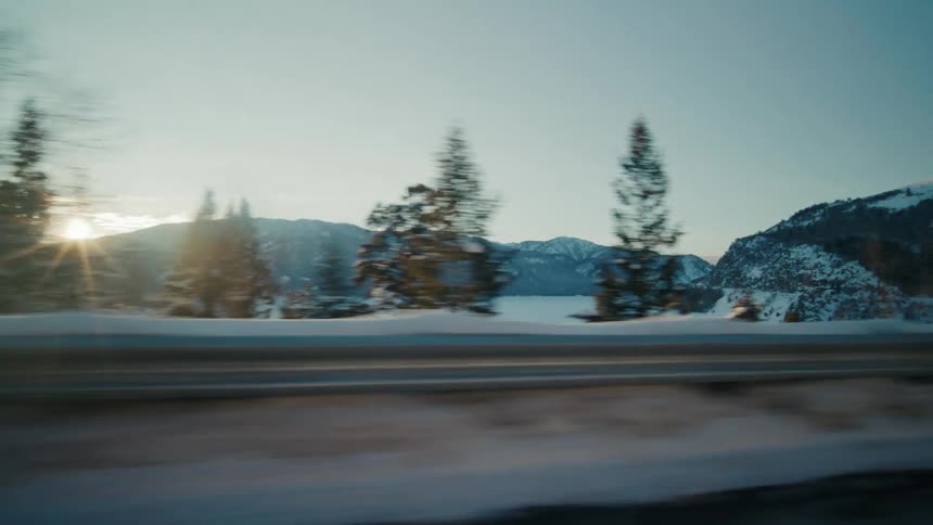 Road passes snow covered hills and valley near mountains on sunny day