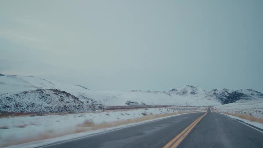Snow covered pastures and fields border highway near mountains