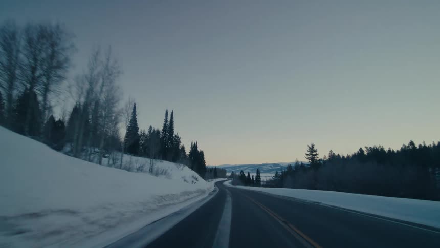 Traveling on a rural highway with snow and trees on the roadside and mountains in the distance