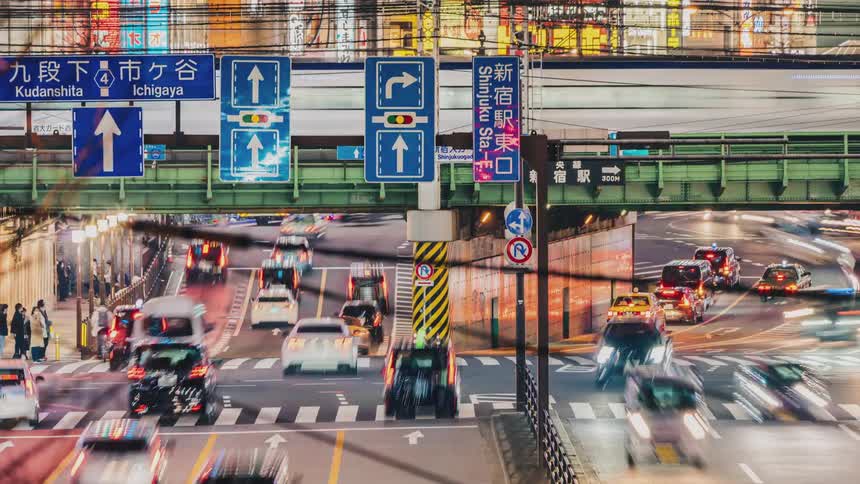 People and traffic pass through a busy intersection under train tracks downtown