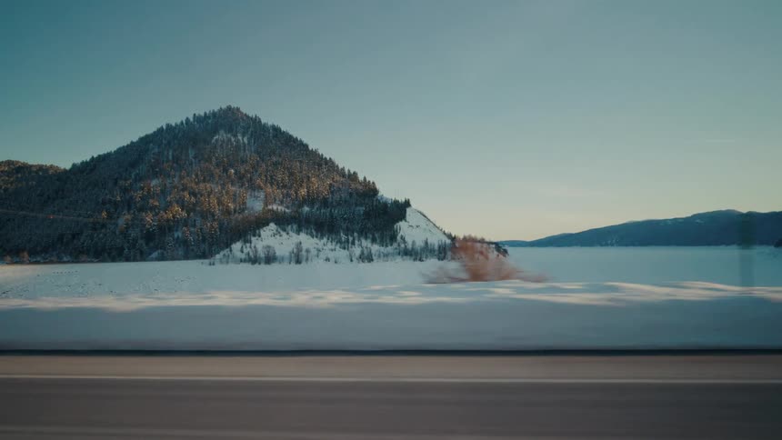 Traveling on a rural highway with snow on the roadside and forested mountains in the distance