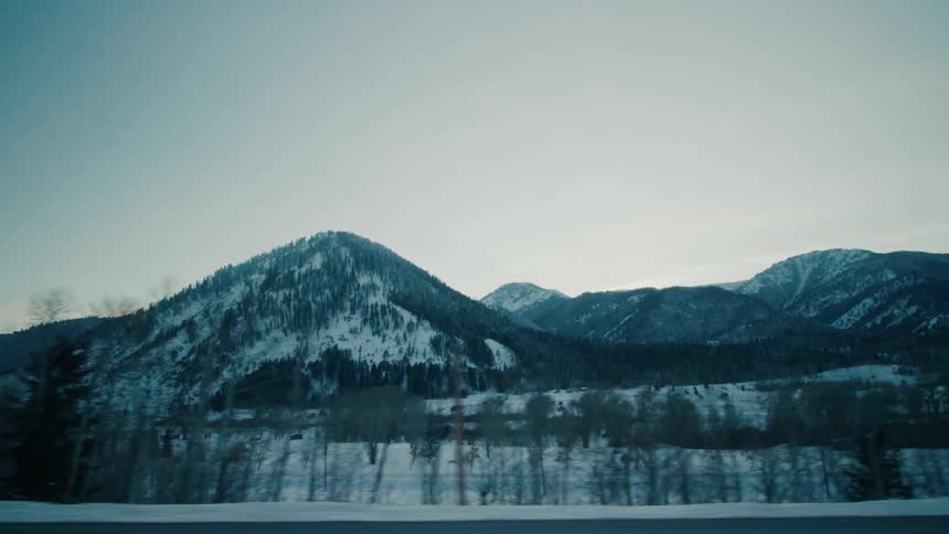 Vehicles drive past snow covered mountains