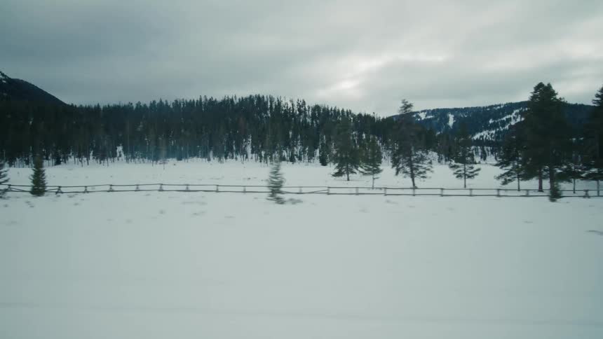 Traveling on a rural highway with snow and a stream along the roadside and forested mountains in the distance