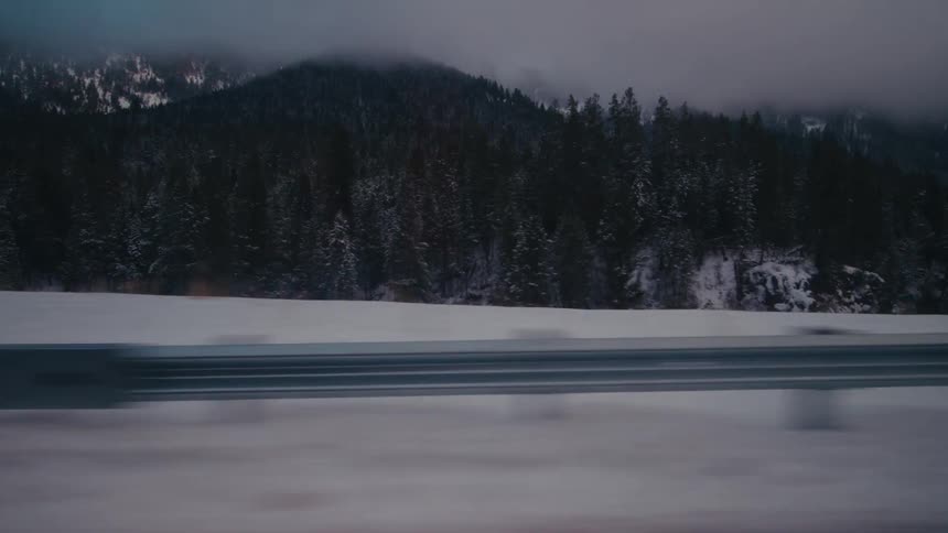 Driving through a wooded area in the snow covered mountains at sunset
