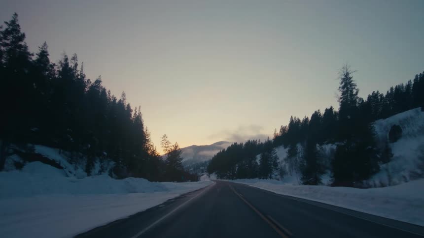 A narrow highway runs past snow covered mountains