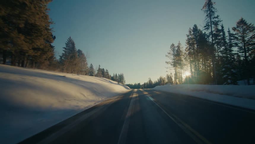 Highway passes between snow and conifer covered slopes on sunny day