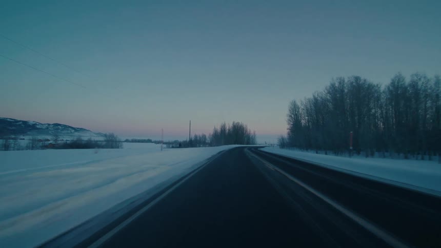 A car is driving on a rural highway during winter