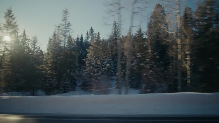 Sun shines brightly in sky as vehicle passes along road near conifer forest covered mountain