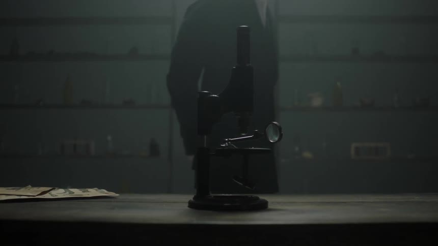 A man walks near a microscope in a dim room