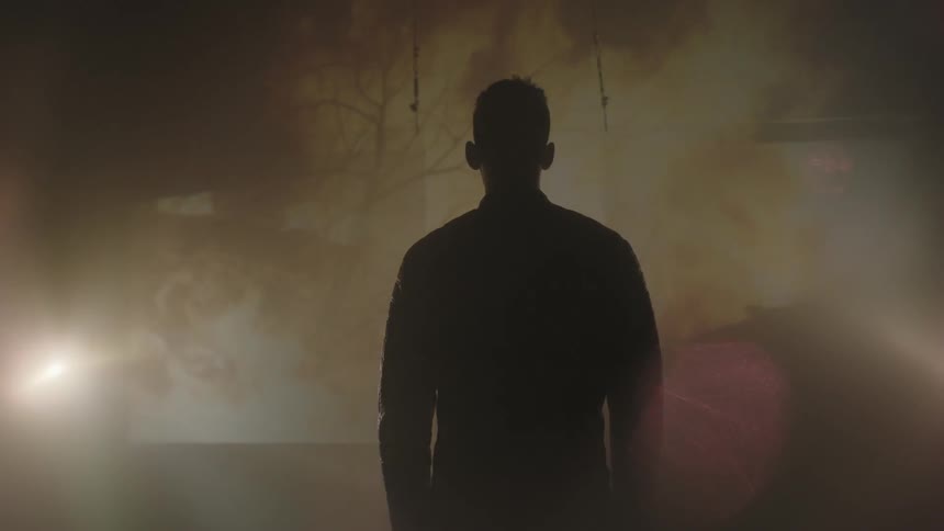 A man standing watching images of a fire projected on screen