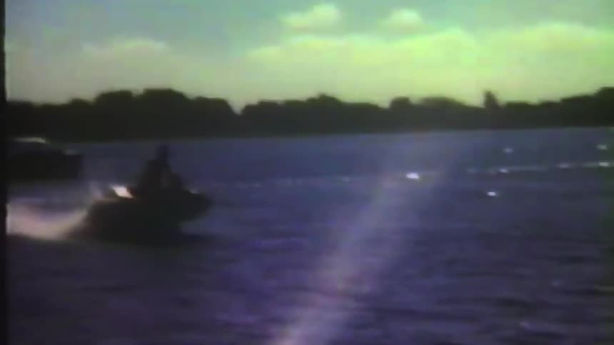 Person rides jet ski across water past boats on sunny day