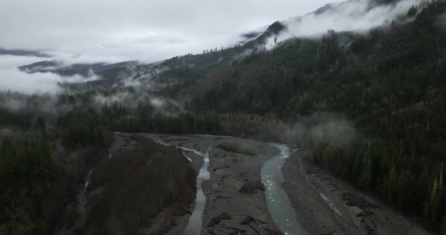 An aerial view of a river flowing through mountains in nature on a cloudy day