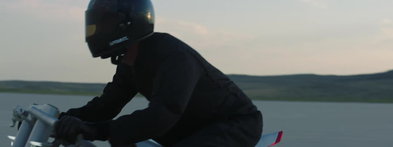 Man wearing a helmet is riding the motorcycle through the desert at dusk