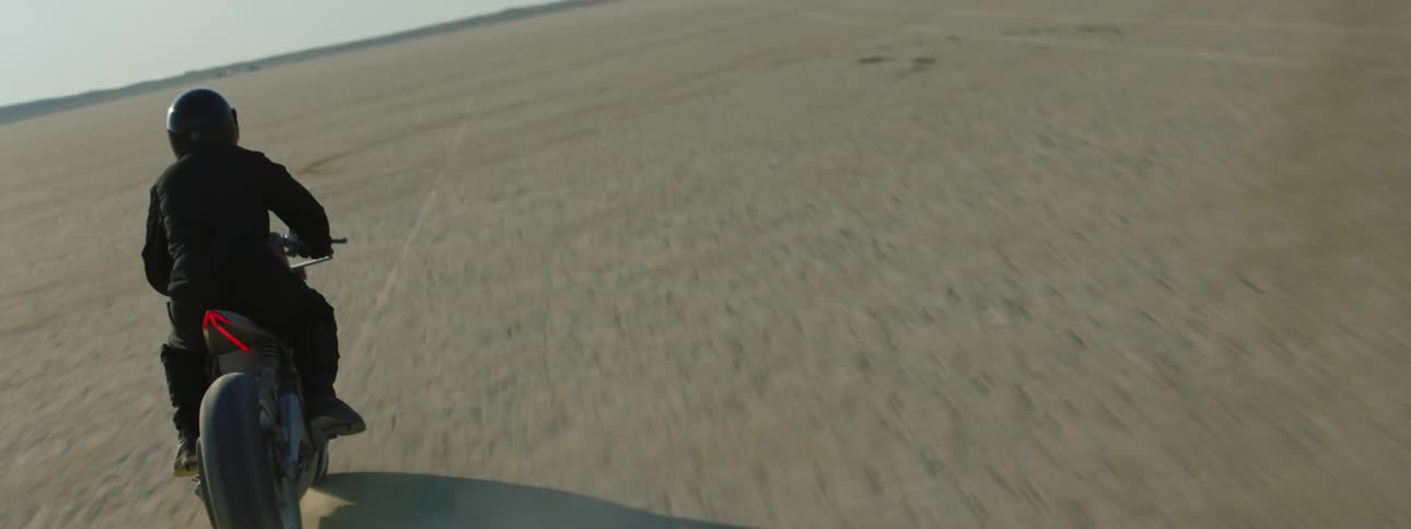 A motorcycle travels across the desert as the rider is wearing a black jacket and helmet