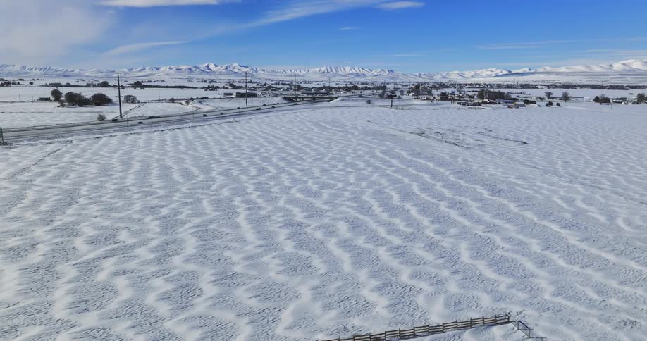 Traffic moves on a rural highway with snow on the ground and snow covered mountains in the distance
