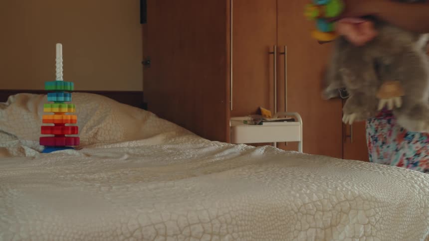 A woman cleans up her childs toys from the top of a bed
