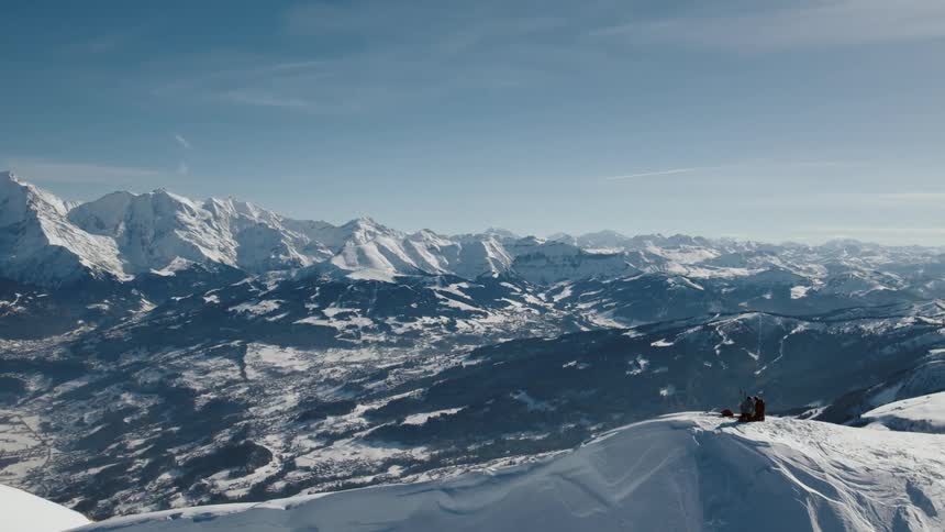 People cluster together on top of summit overlooking valley surrounded by snowy mountains