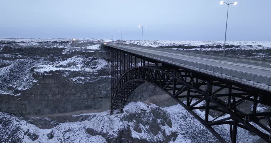 An aerial view of vehicles traveling over an arch bridge on a snowy morning