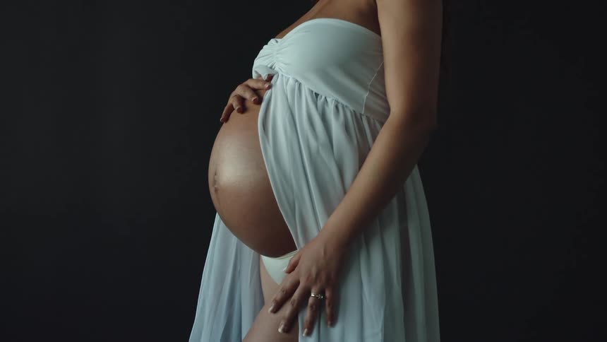 A woman rubbing her pregnant belly while wearing a white dress