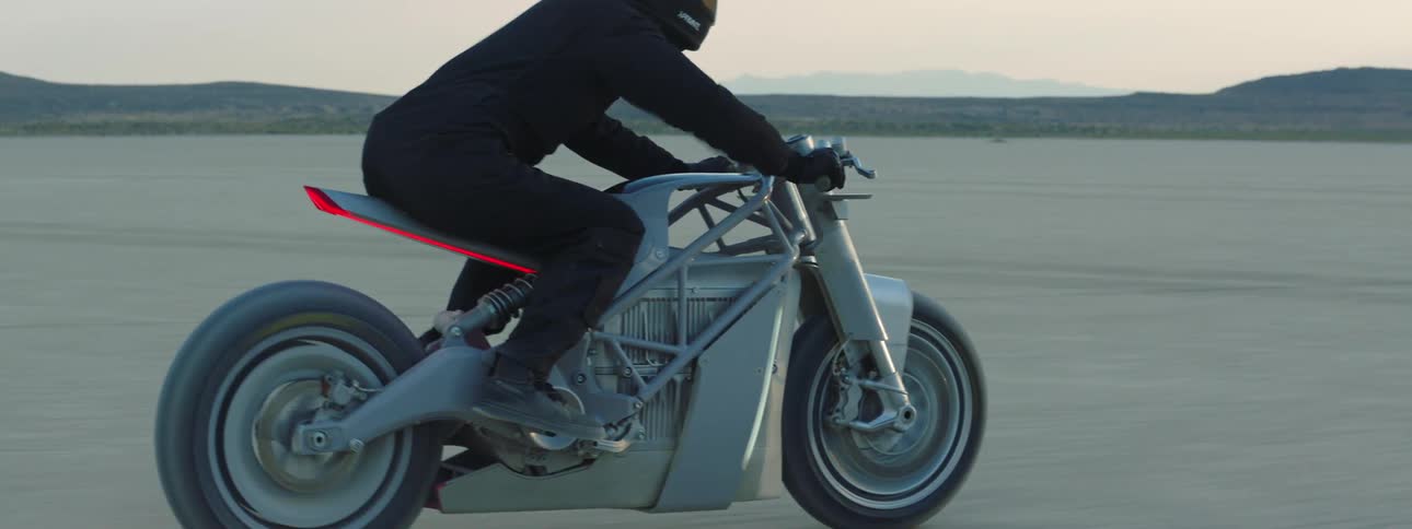 Motorcyclist wearing helmet rides motorcycle across flat desert with mountains in the background