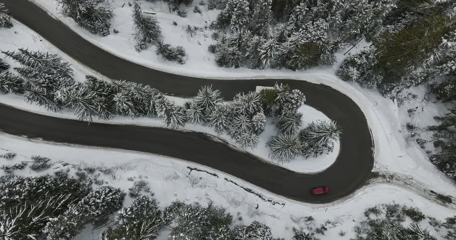 Aerial view of car red car and white minibus driving on winding road in the snowy field